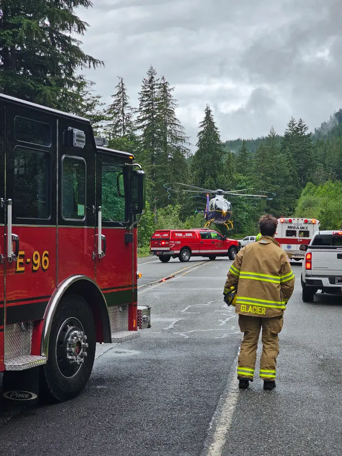 Glacier engine E-96 on a wet highway while a medevac helicopter lands beyond the ambulance